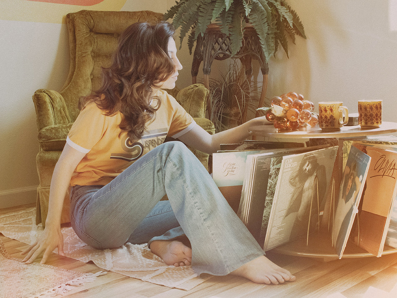 Woman Sitting next to Vinyl Records Wearing Graphic 1970’s Style Ringer T-Shirt with Suspended In Time Song Lyrics from Xanadu Movie